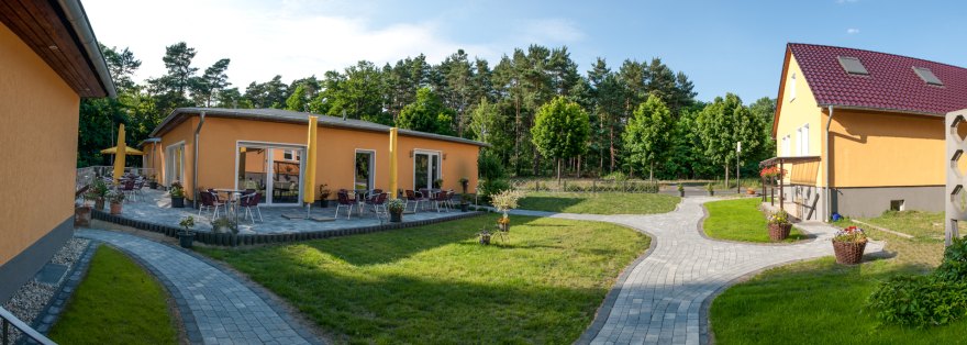 Die Häuser der Pension Traumfänger mit Terrasse, Rasenfläche und Kiefernwald im Hintergrund